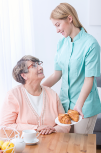 A healthcare worker bringing breakfast to a senior woman at a table