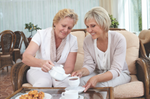Two senior women enjoying a cup of coffee together on a couch