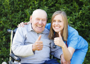 A senior man in a wheelchair and healthcare worker giving thumbs up
