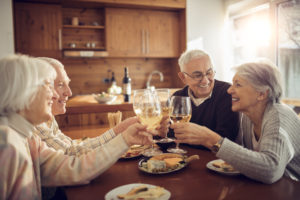 Four seniors smiling while having a glass of wine at lunch