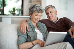 A senior couple sitting on the couch looking at a tablet together