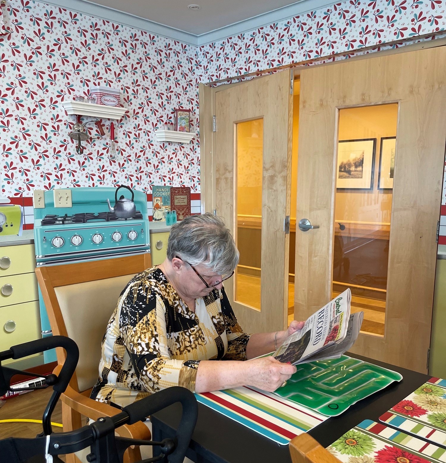 A resident reading a newspaper in front of a Sensory-scapes mural depicting a 1950s kitchen