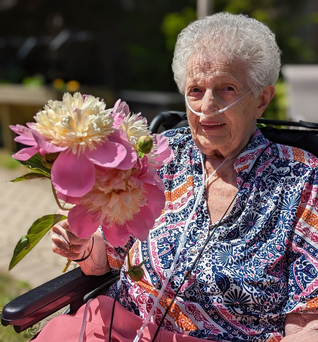A peopleCare resident smiling while holding a flower outside
